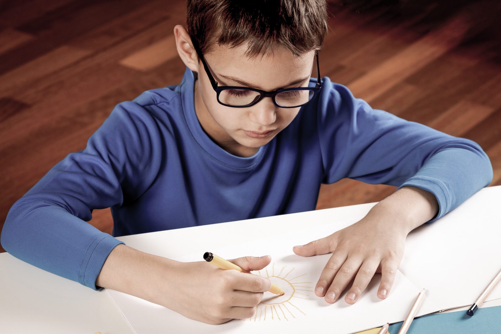 A boy in spectacles bent close over his writing at a desk