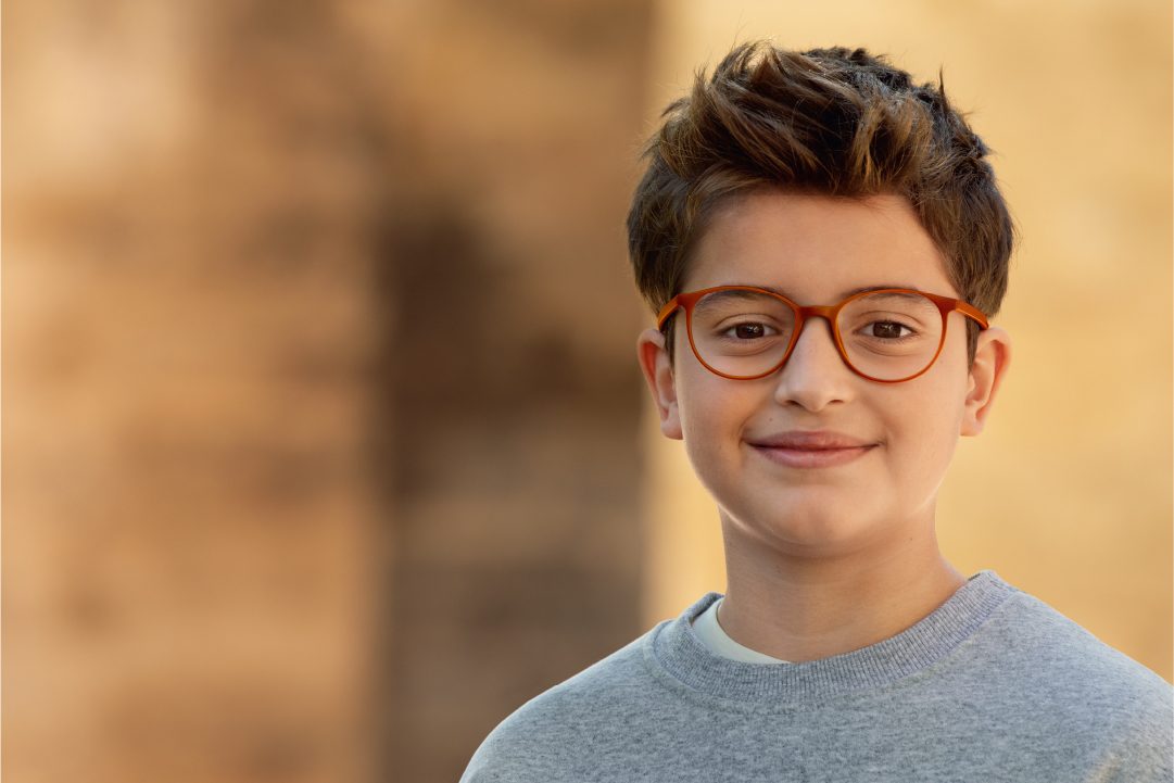 A boy wearing red-framed MiYOSMART spectacles, smiling after his lens fitting
