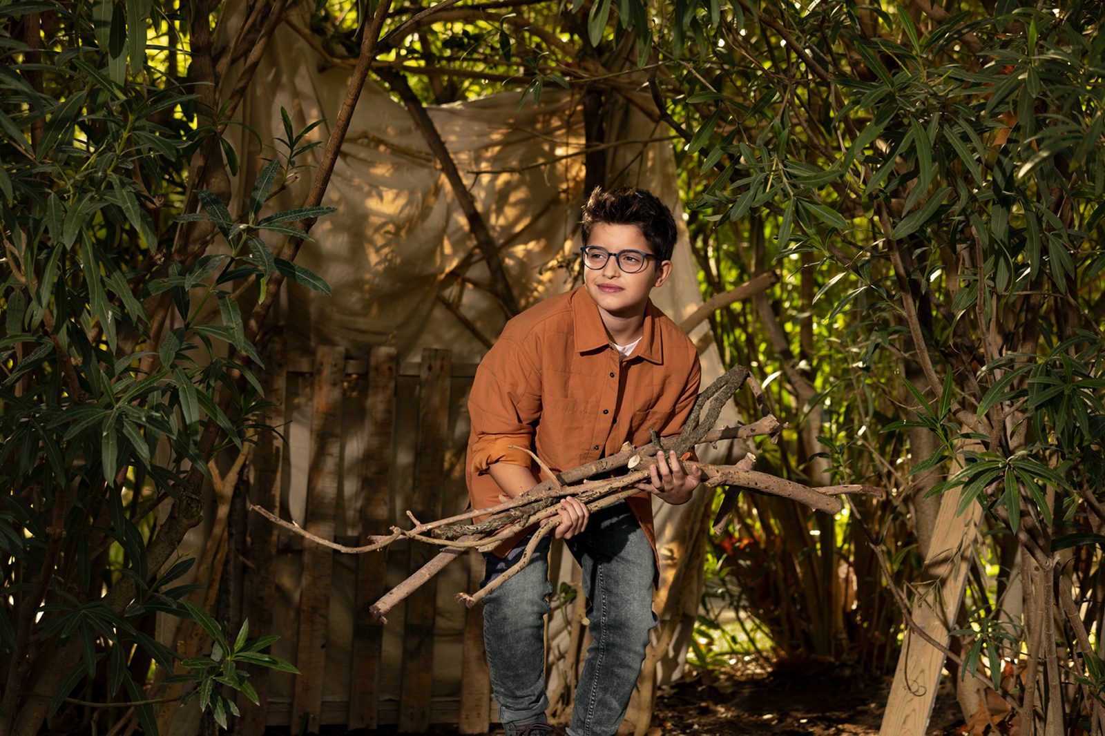 A boy in MiYOSMART spectacles building a den among the trees