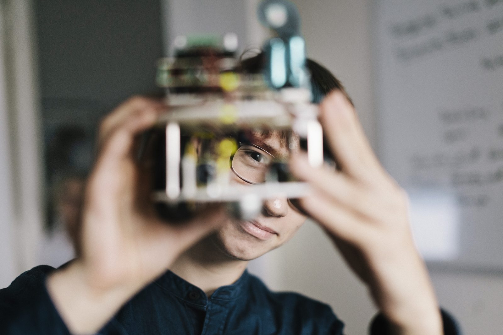 A child in spectacles holding an electronics project up close to their face to inspect it