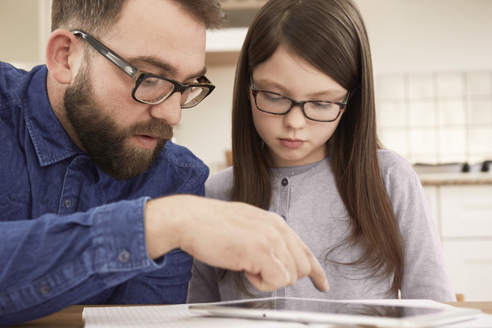 A father and his daughter, both wearing spectacles, looking at a tablet together