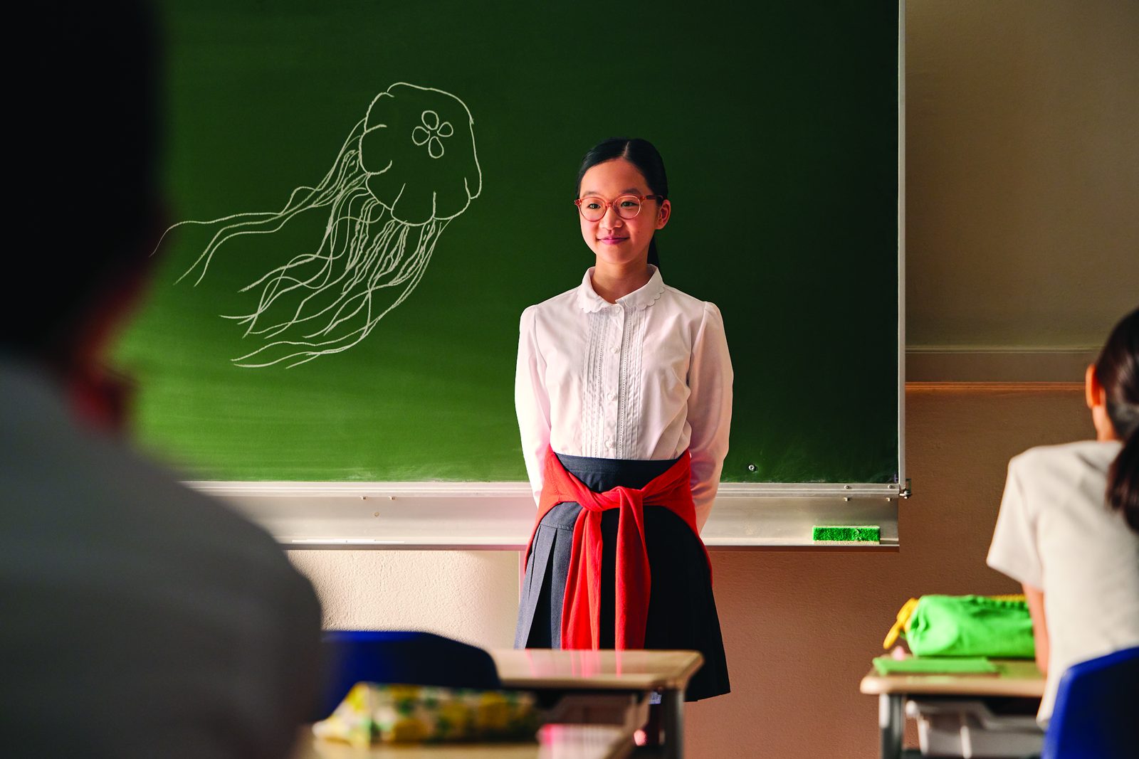 A girl in MiYOSMART spectacles presenting at the blackboard in her classroom