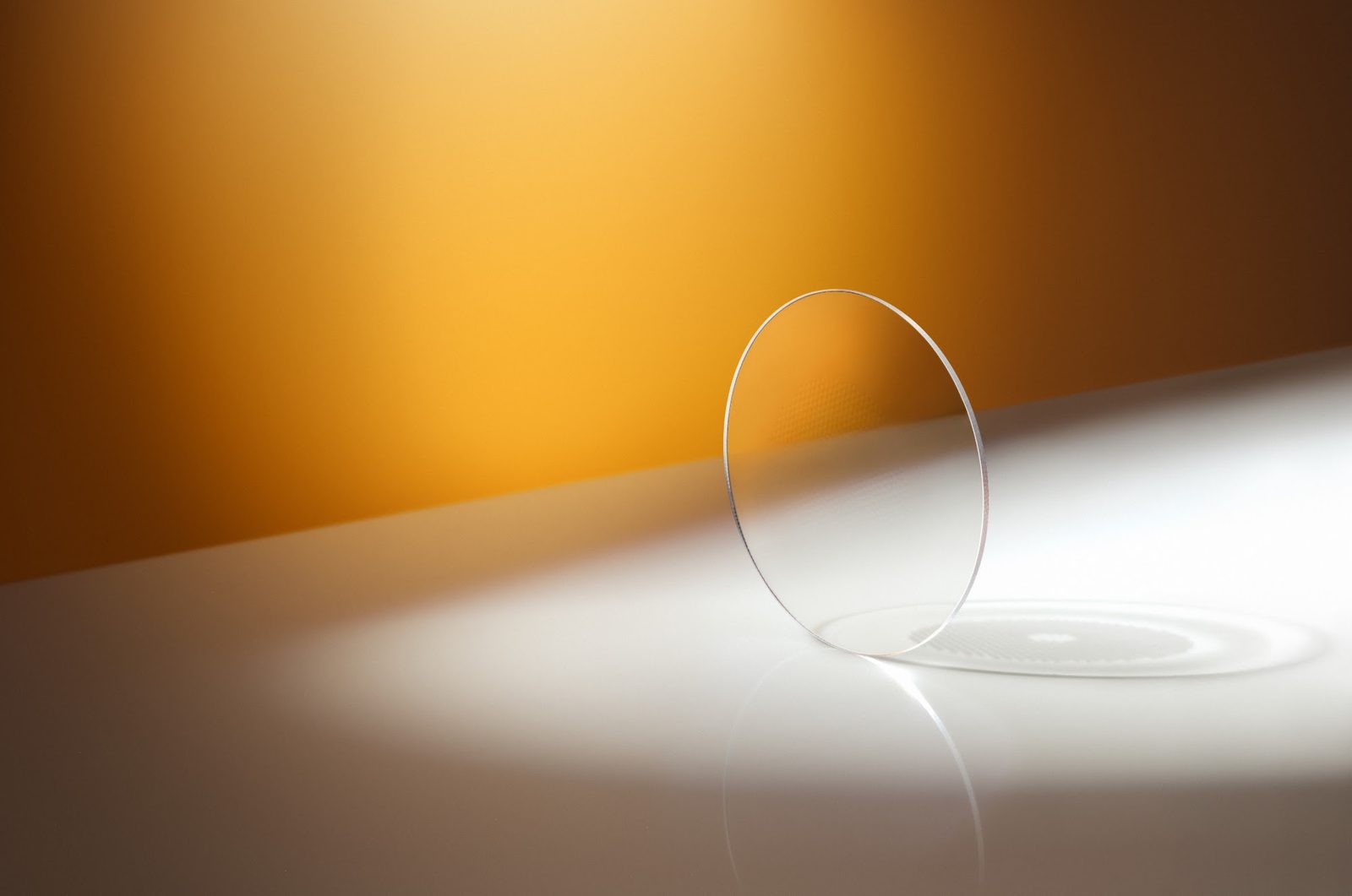 A MiYOSMART iQ lens standing on edge in warm light, showing its slim edge profile