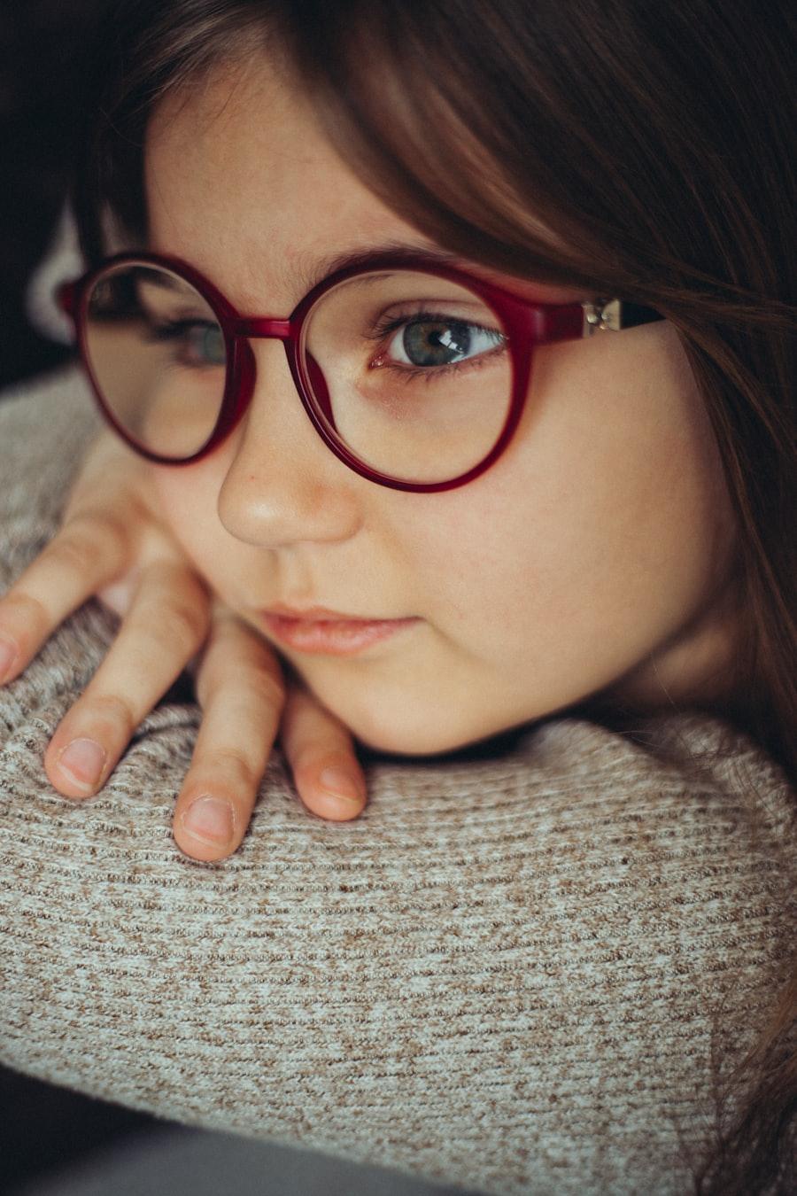 A girl wearing red-framed spectacles resting her chin on her hands